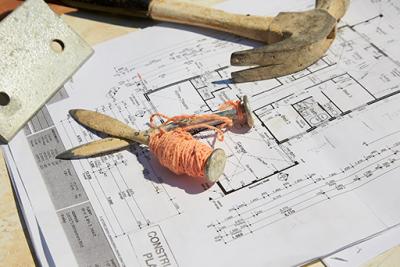 Image of building plans with hammer and pegs and string.