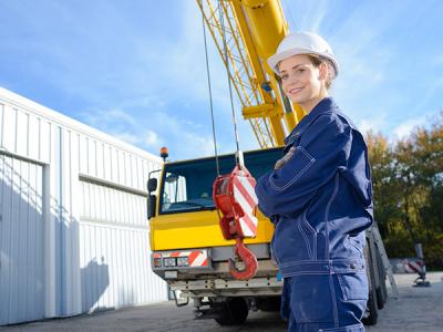 Young woman in hard hat standing in front of mobile crane