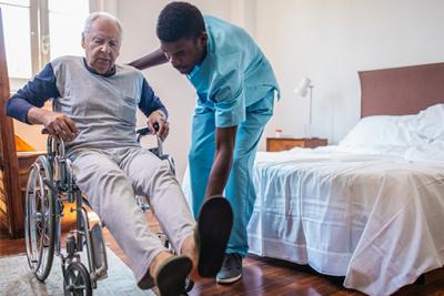 Male in a wheelchair with male care assistant helping him.