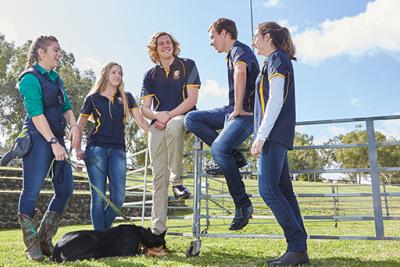 Group of young students chatting around a paddock fence with a dog.