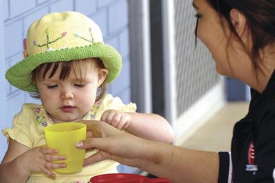Young toddler being handed a cup by a childcare worker.