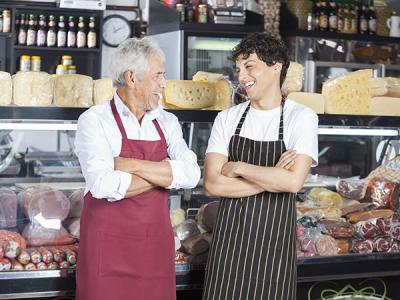 Two smallgoods staff laughing in front of deli counter stocked with meats