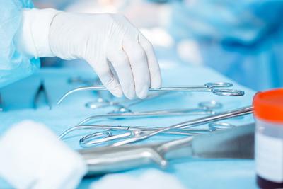 Nurse with gloves and gown selecting surgical equipment from table.